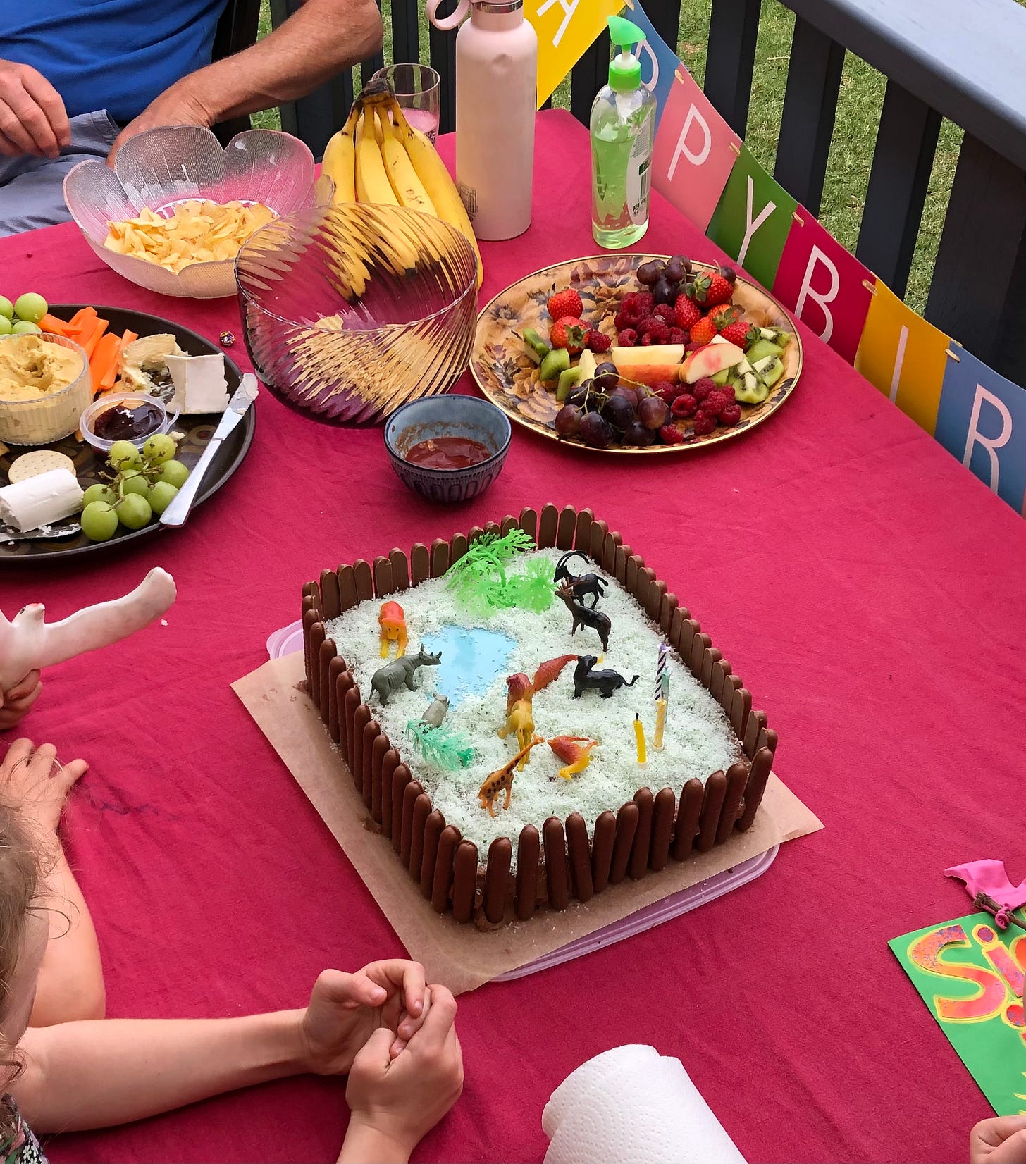 children's zoo birthday cake in centre of a table surrounded by hopeful children's reaching hands