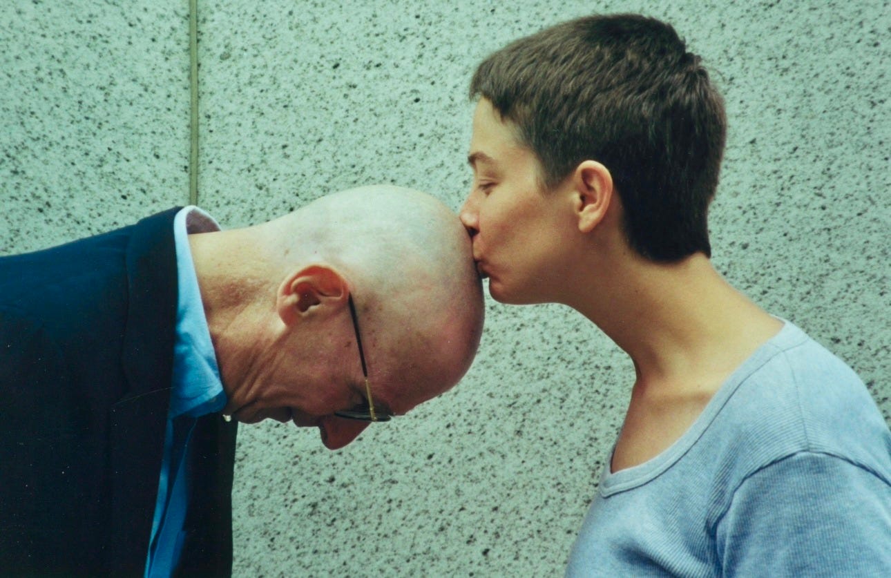 girl with buzz cut kisses top of her father's head bald from chemo