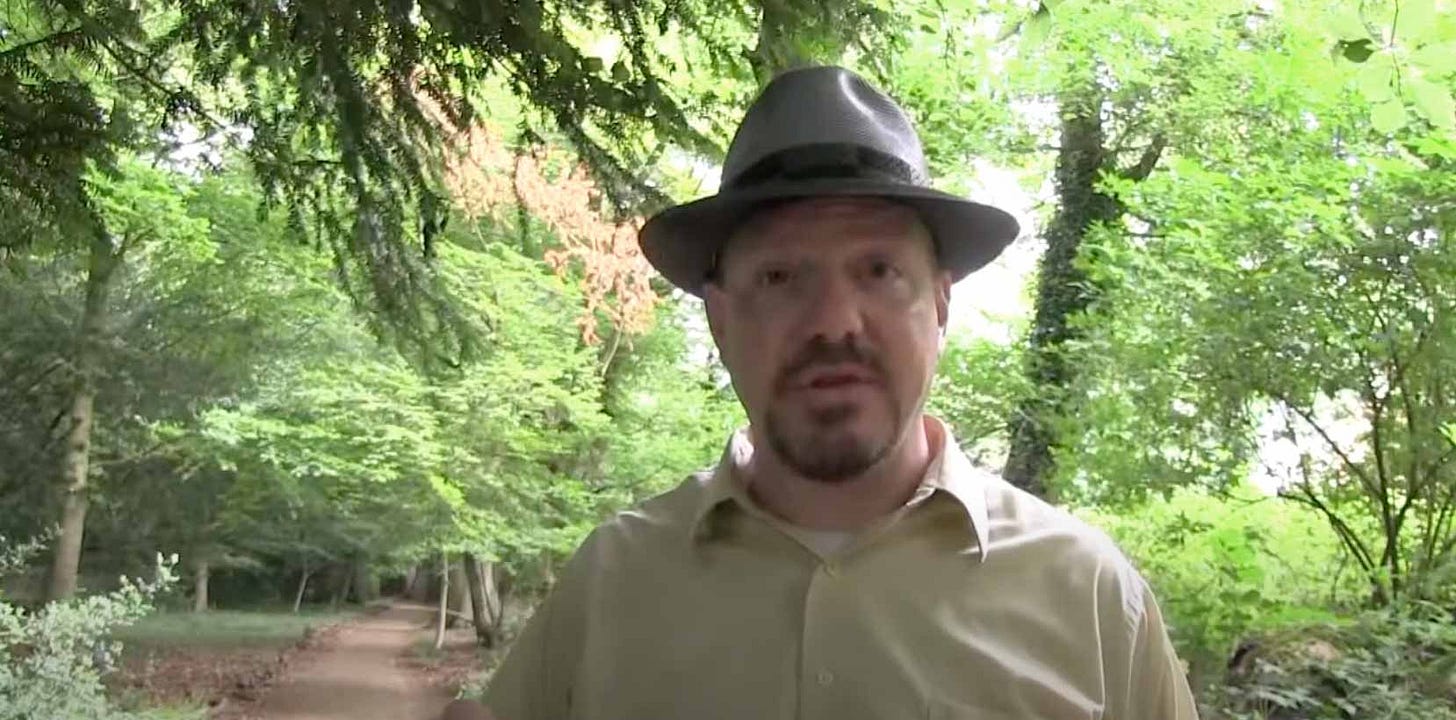 John Hawks seen talking in front of a wooded background with a sandy pathway