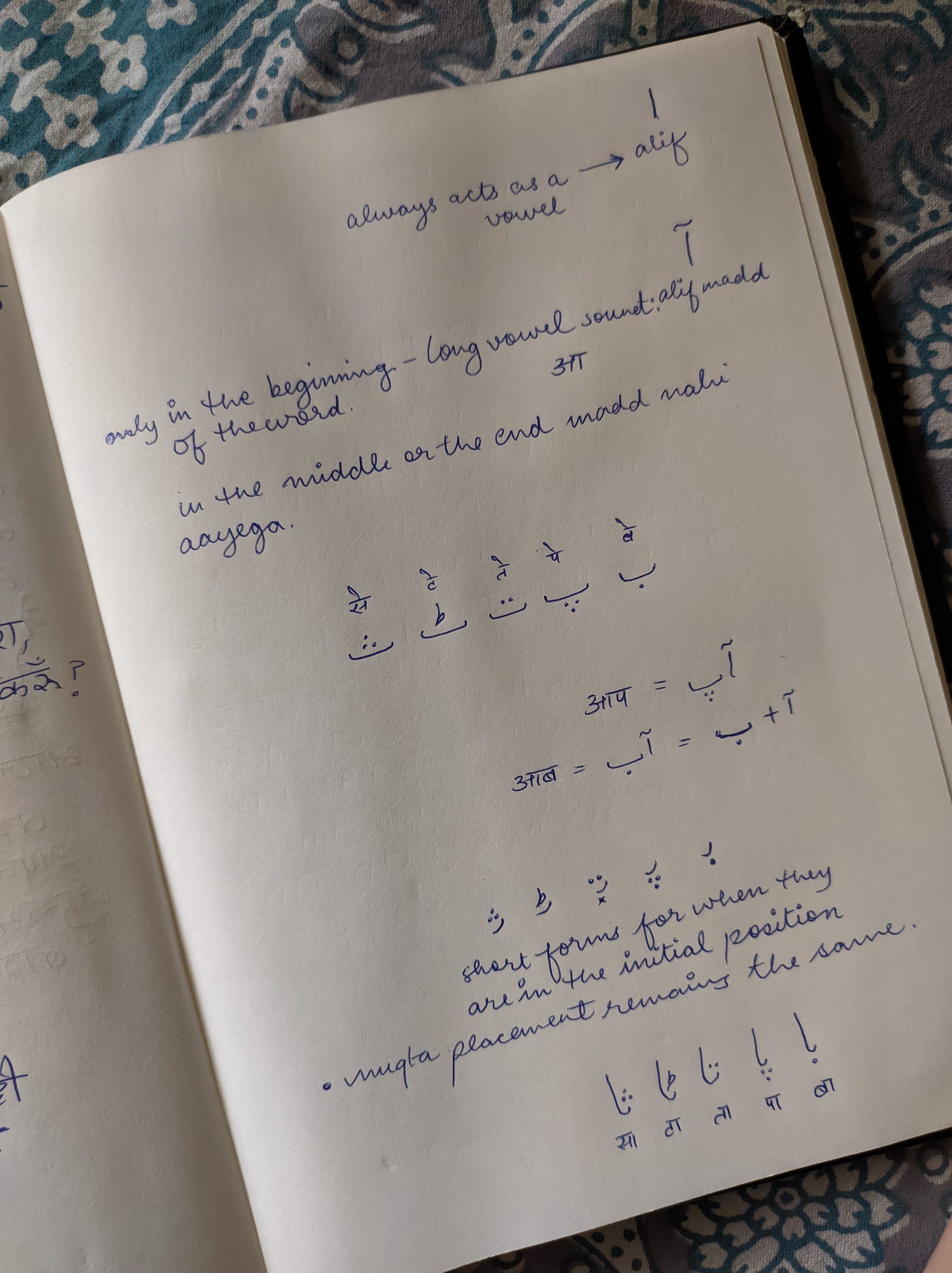 The Urdu alphabet written on a white notebook page with notes scribbled below them. 