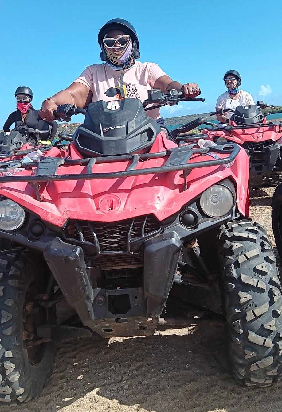 A black woman is sitting on the seat of a red ATV, wearing a black helmet and purple face covering.