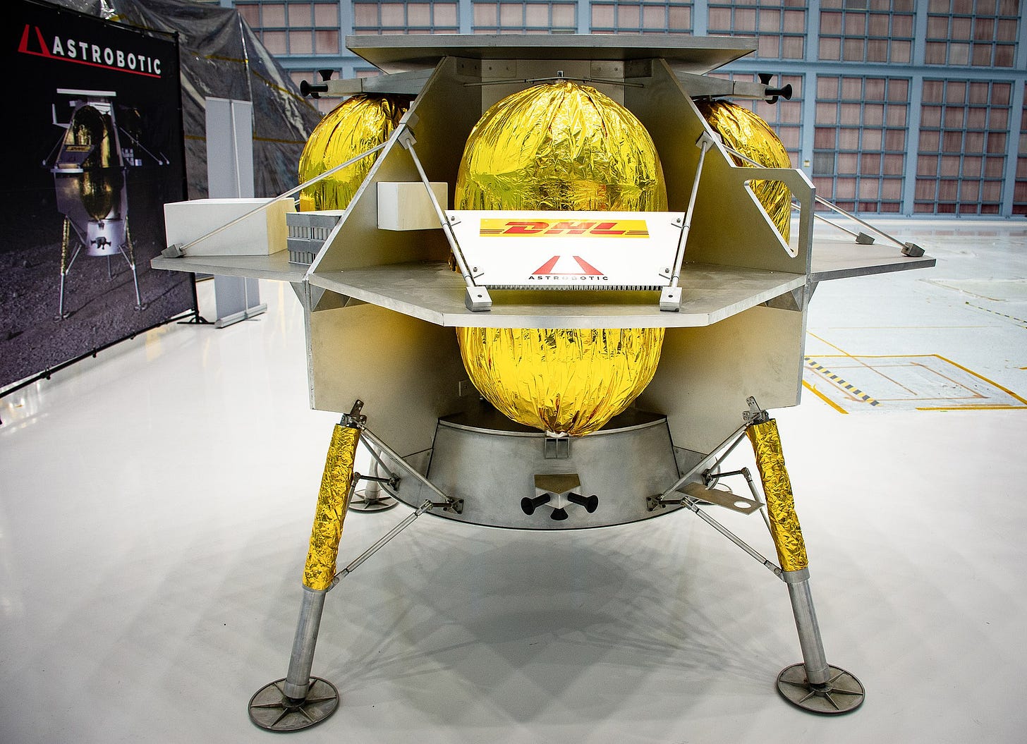 In a factory, a high-tech lunar lander. A metallic structure on four legs with yellow foil balloon looking compartments