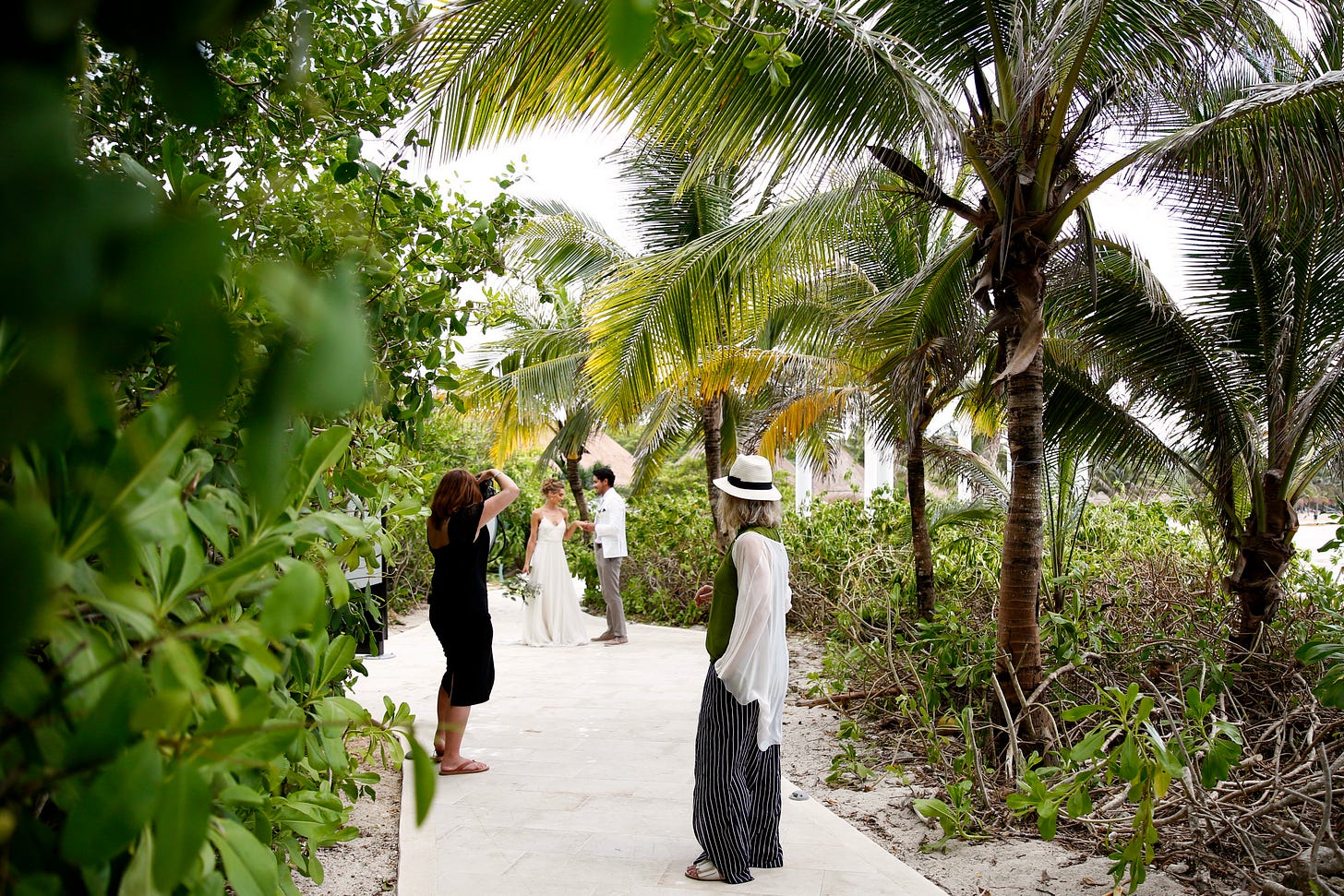 Karen Bussen art directs a photo shoot with a wedding theme in a palm-tree lined park in Mexico. A bride and groom hold hands among the green leafy foliage