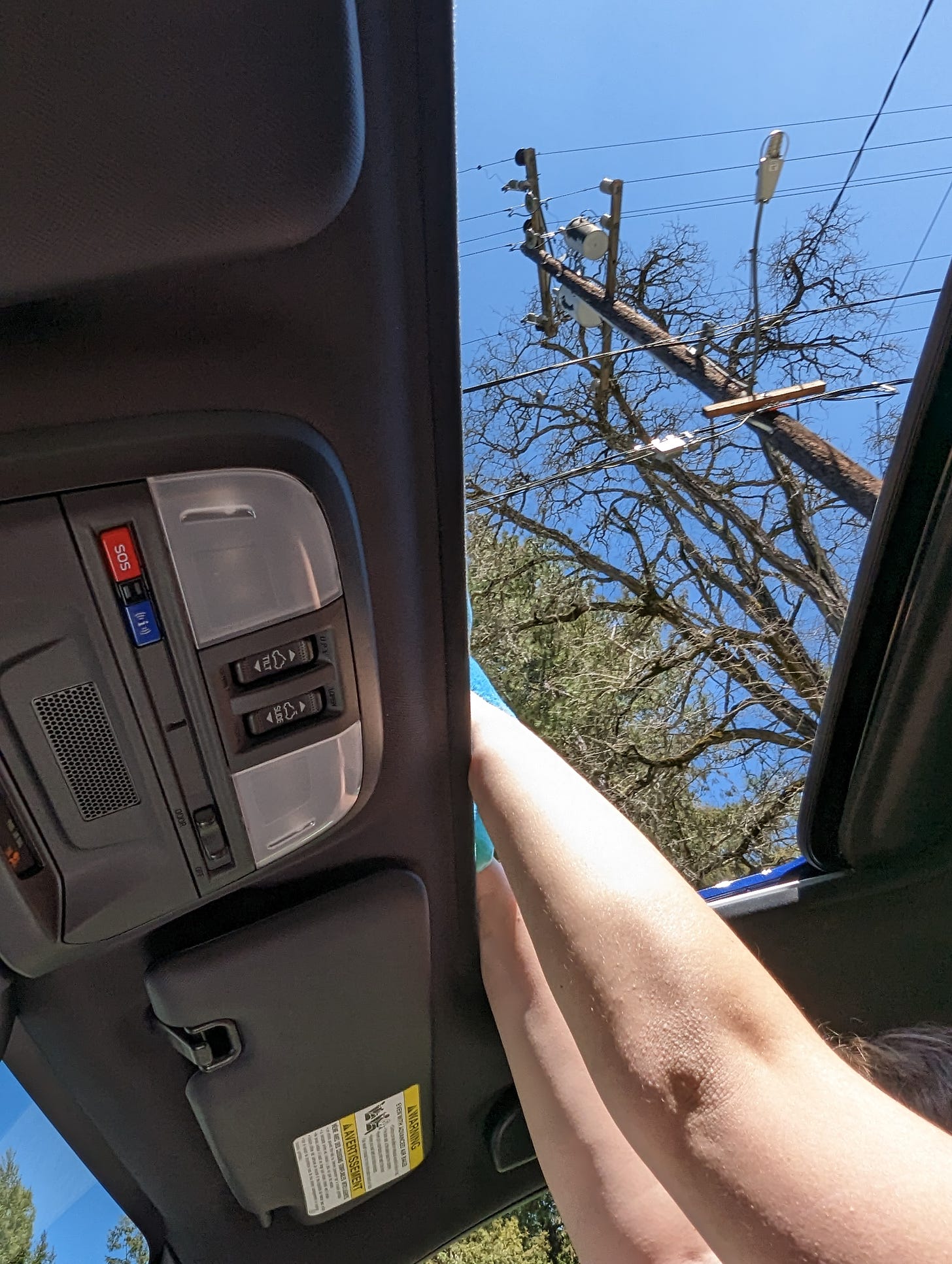 photo from inside a car showing a pair of arms reaching above and through the sunroof with a tiny bit of blue stuffed animal showing
