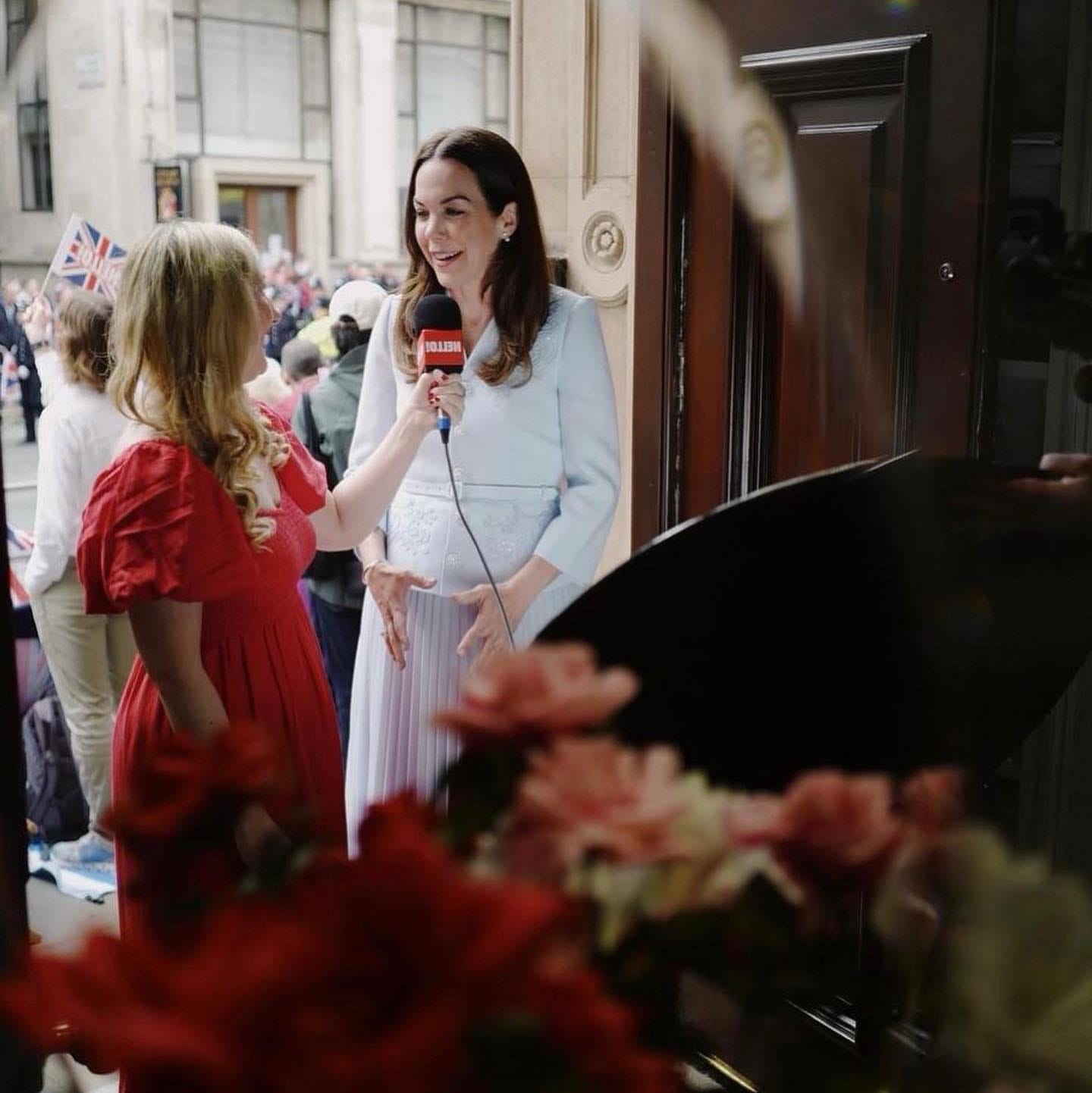 Isabelle Casey in a red dress interviewing Elizabeth Holmes at King Charles's coronation