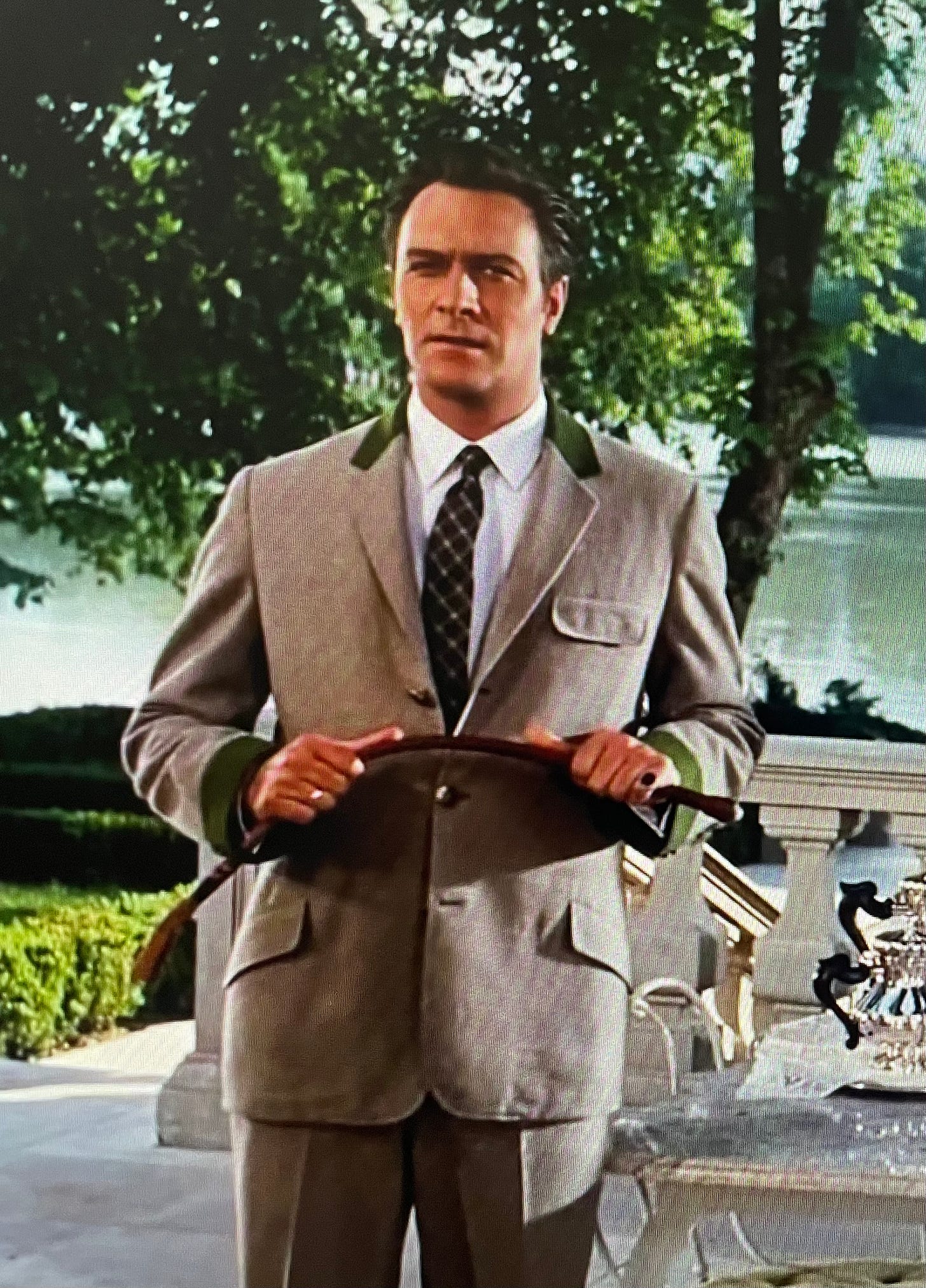 Captain Von Trapp holds a riding crop in both hands, bending it slightly, while looking stern
