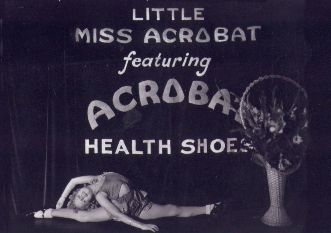 A black-and-white photo of an eleven-year old girl in dance clothes doing the splits and bending backwards in front of a banner that reads, "Little Miss Acrobat featuring Acrobat Health Shoes."