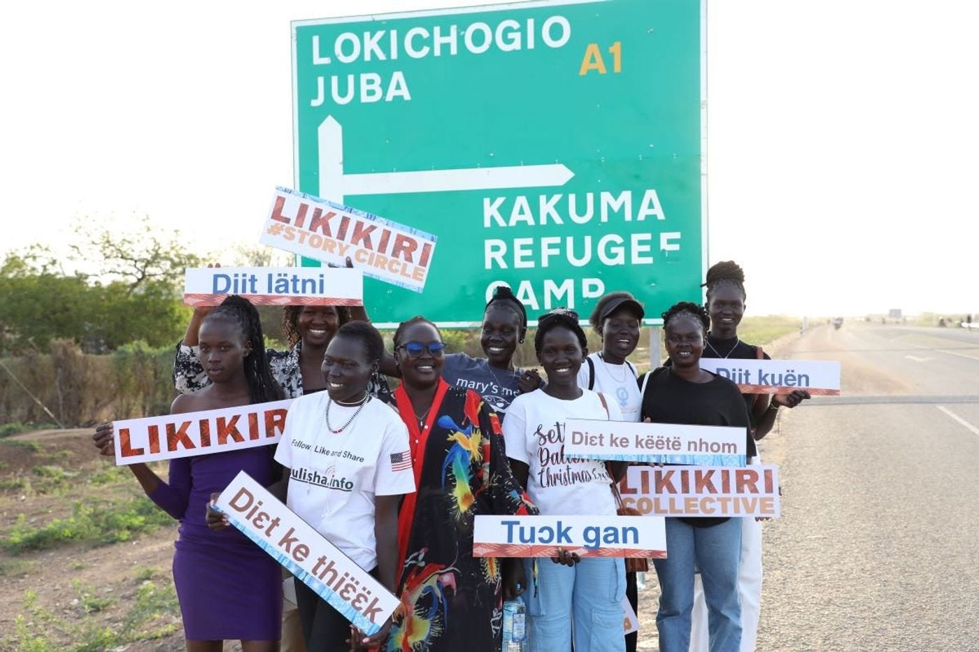 Een groep vrouwen staat voor een straatbord dat de weg wijst naar Juba, Zuid-Soedan en het vluchtelingenkamp Kakuma, Kenia.