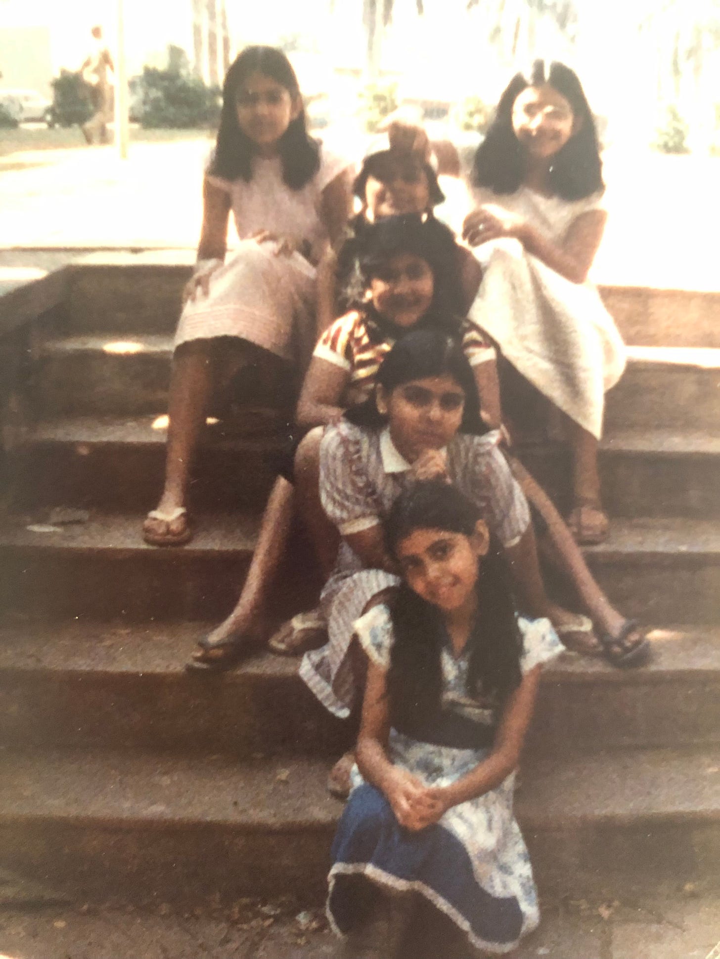 Six Indian girls in dresses and skirts sitting on outdoor steps.