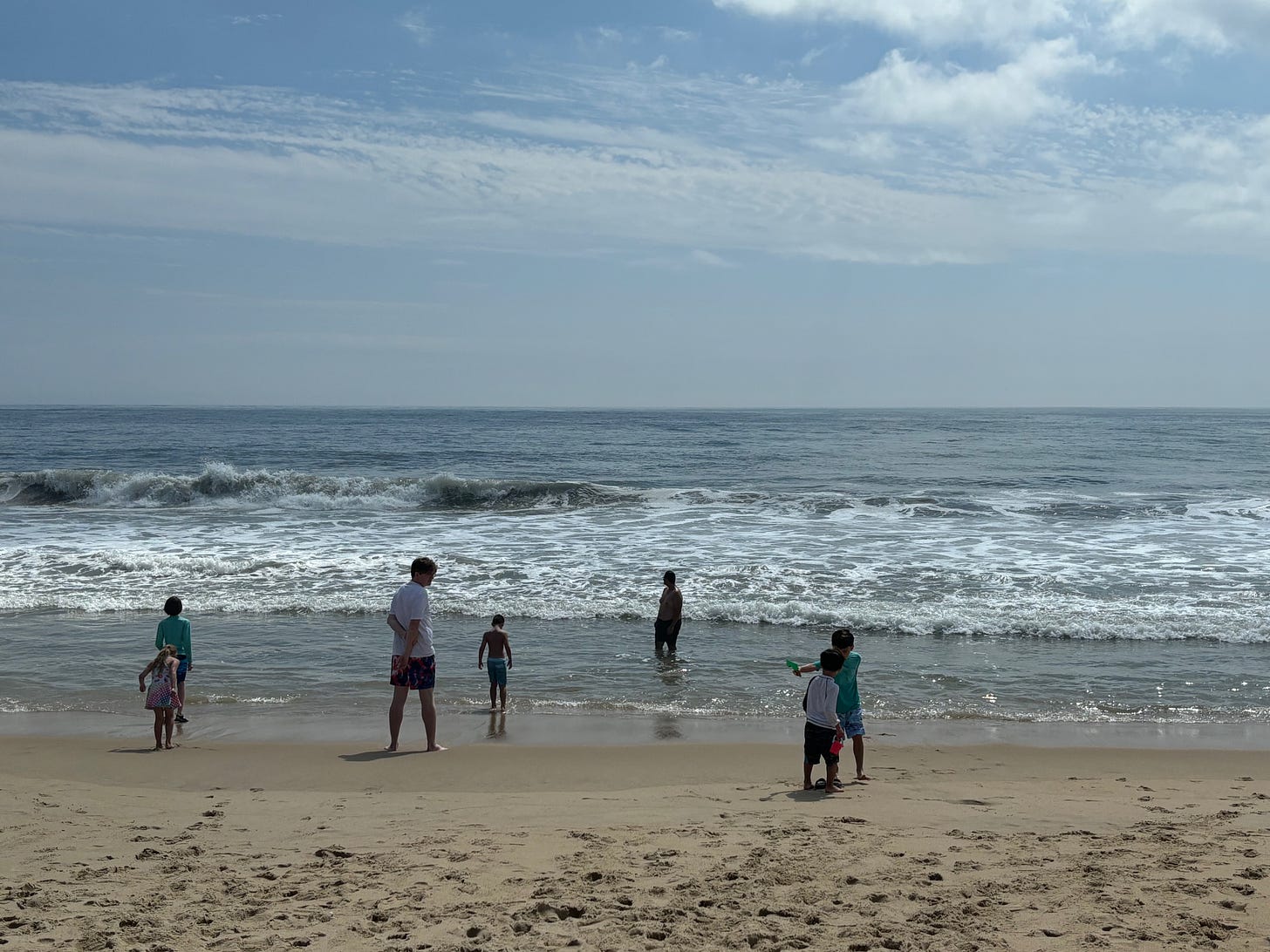 Several kids and two adults standing at the beach in Ocean City, with a blue sky above