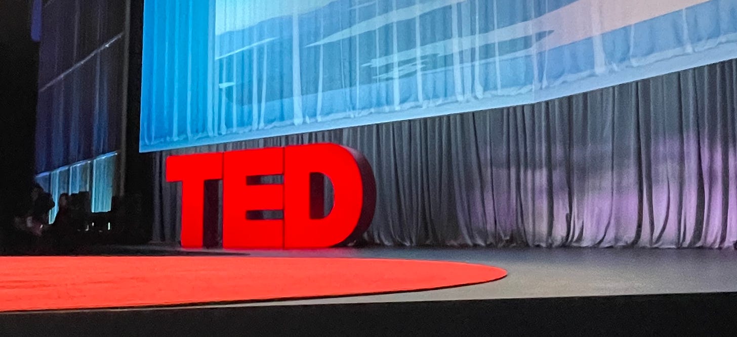 A photograph of the TED stage with the red dot and red TED letters at eye level.