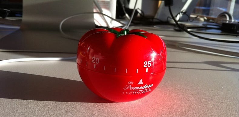 photo of a red timer shaped like a tomato sitting on a desk with computer cables in the background