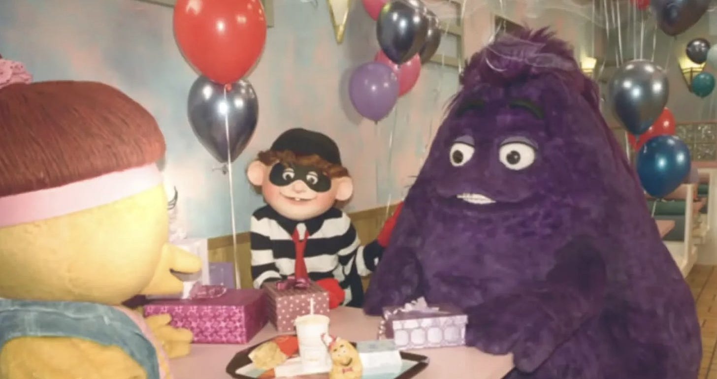 An older-looking photo of Grimace–the giant purple creature and McDonald’s mascot–at what appears to be his birthday party in a McDonald’s store. His eyes are vacant, and stare back at you through the screen. He does not fear death. Perhaps you should. 
