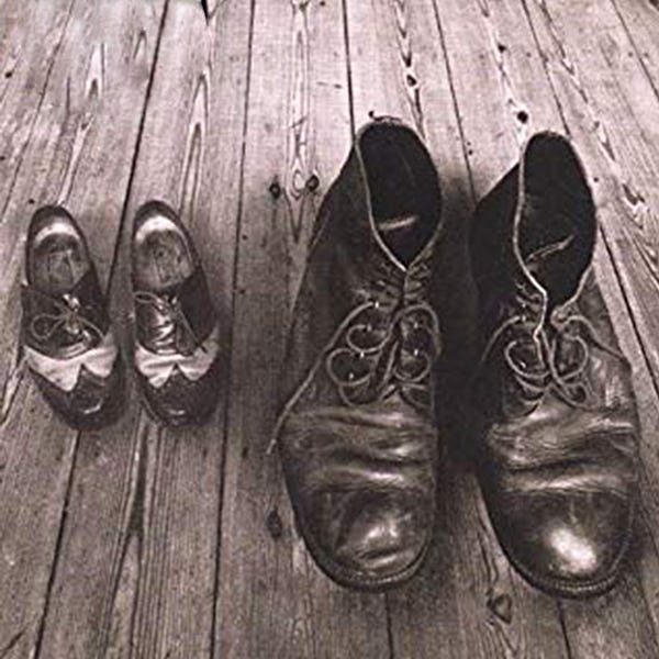 Two sets of shoes on a wooden floor: a small women's pair and an enormous men's pair.