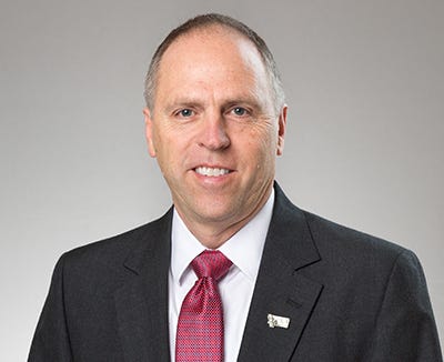 man in suit and red tie smiles against a grey background