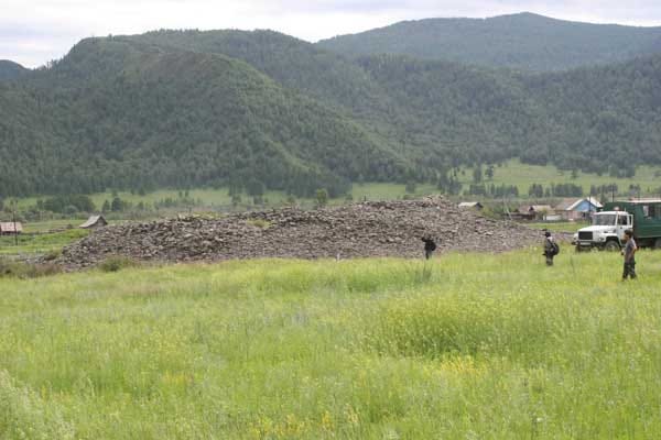 Large mound of rocks with grass surrounding and mountains in background
