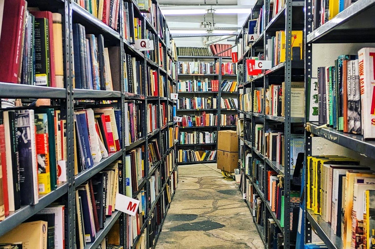 View of a bookstore corridor, with shelves on both sides and on the background, full of books.