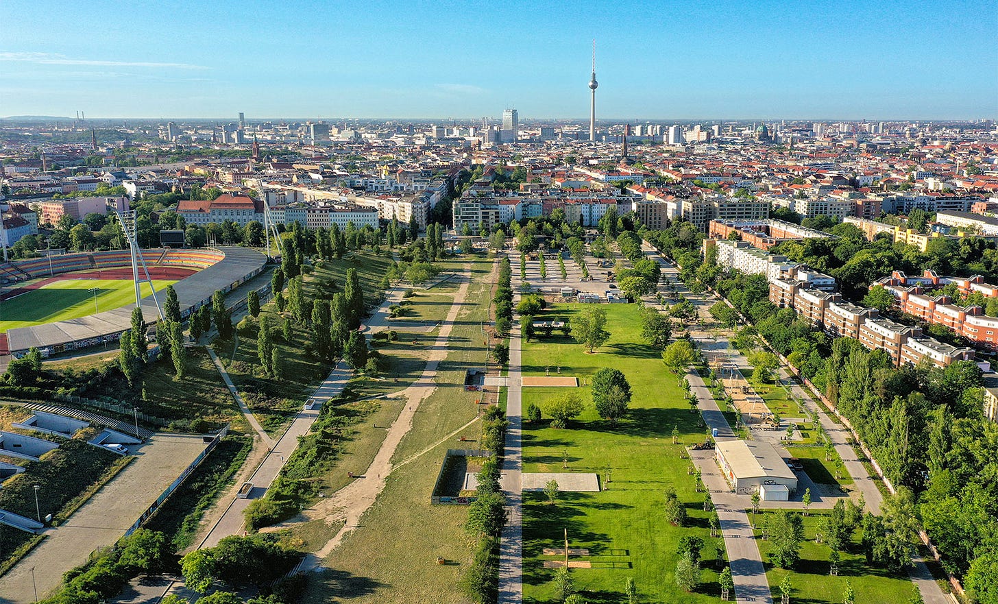 Imagem aérea do Mauerpark, um parque retangular, bem gramado de um lado e menos do outro. Há um ginásio aberto na lateral e se vê a Torre de TV em Berlim