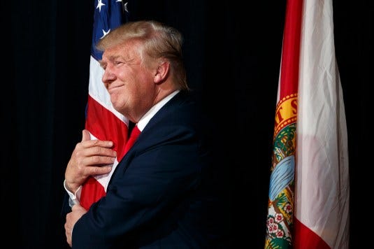 Republican presidential candidate Donald Trump hugs a the American flag as he arrives to speak to a campaign rally, Monday, Oct. 24, 2016, in Tampa, Fla. 