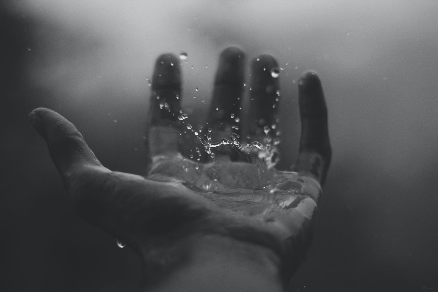 A raindrop splashes in someone's left hand. The picture is black and white.