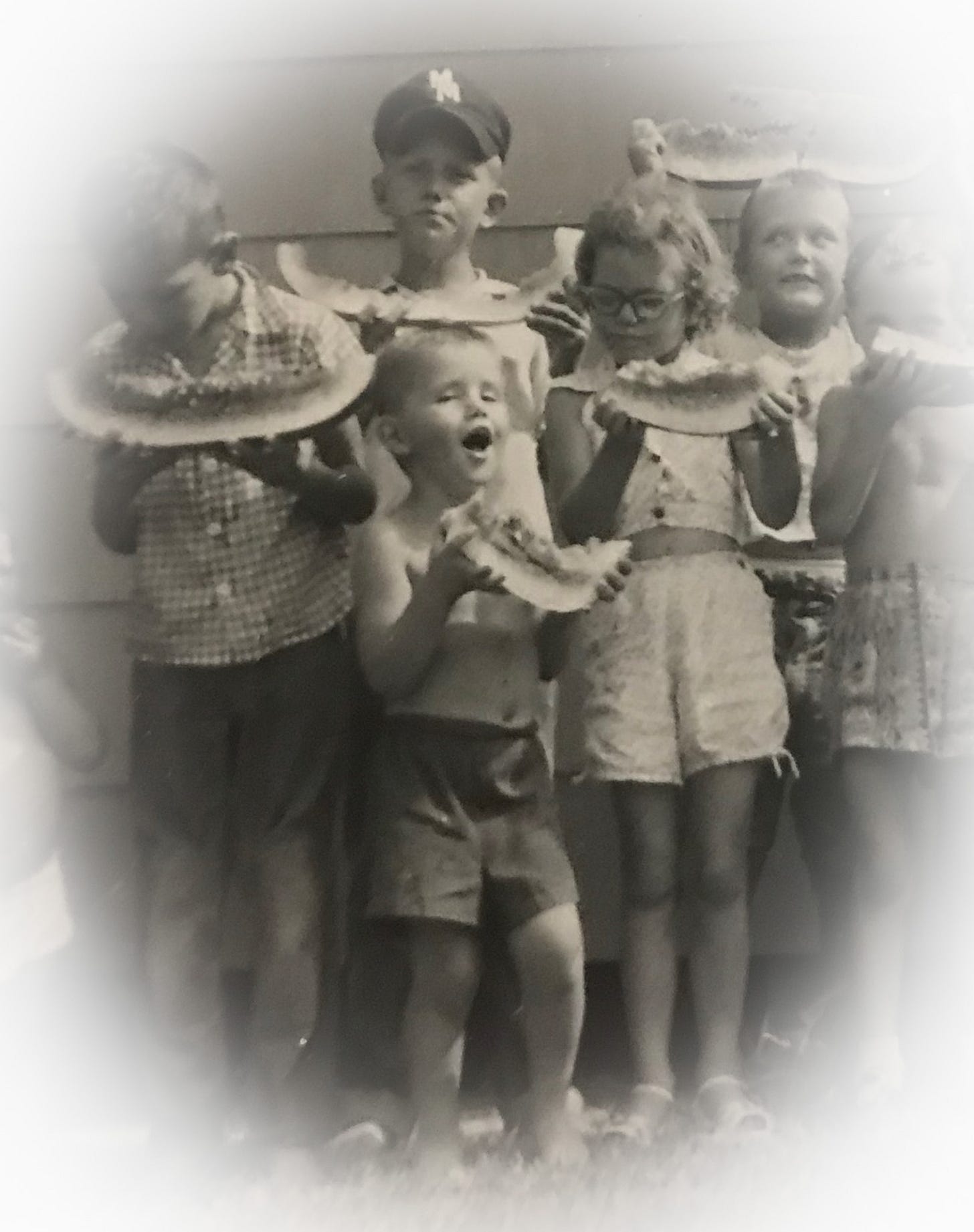 Black and white photo from the 1950s of young children, boys and girls, lined up holding slices of watermelon