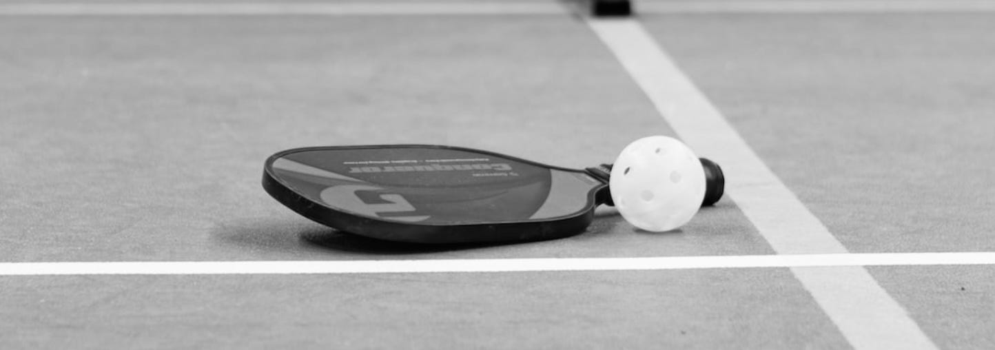 Pickleball paddle and ball sitting on a pickleball surface, a sport that unites men and women.