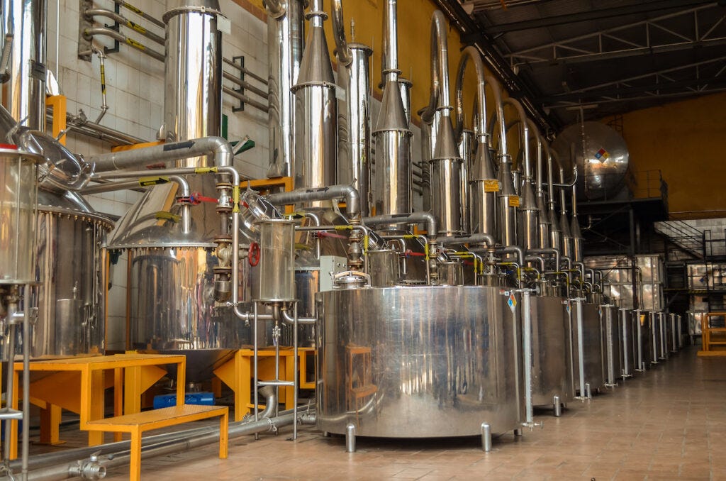 Industrial machinery used for tequila distillation, featuring large metal stills and interconnected pipes in a modern distillery setting. Industrial machinery used for tequila distillation, featuring large metal stills and interconnected pipes in a modern distillery setting.