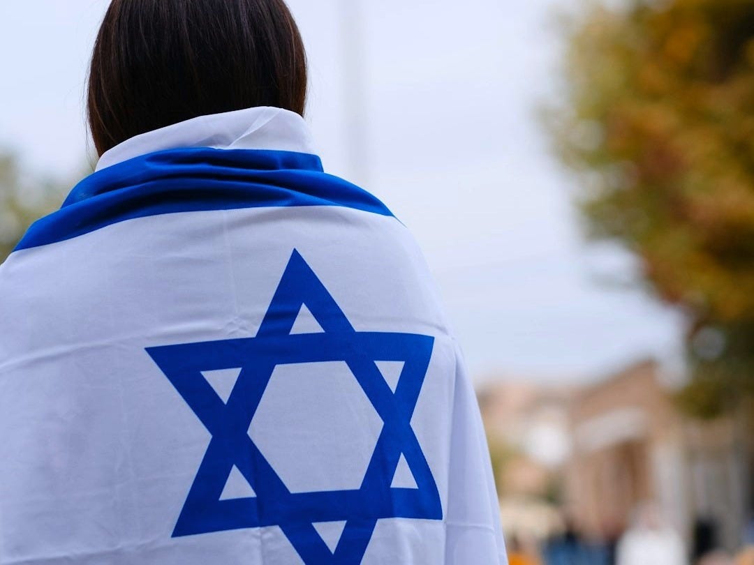 woman in white and blue hoodie standing near green trees during daytime