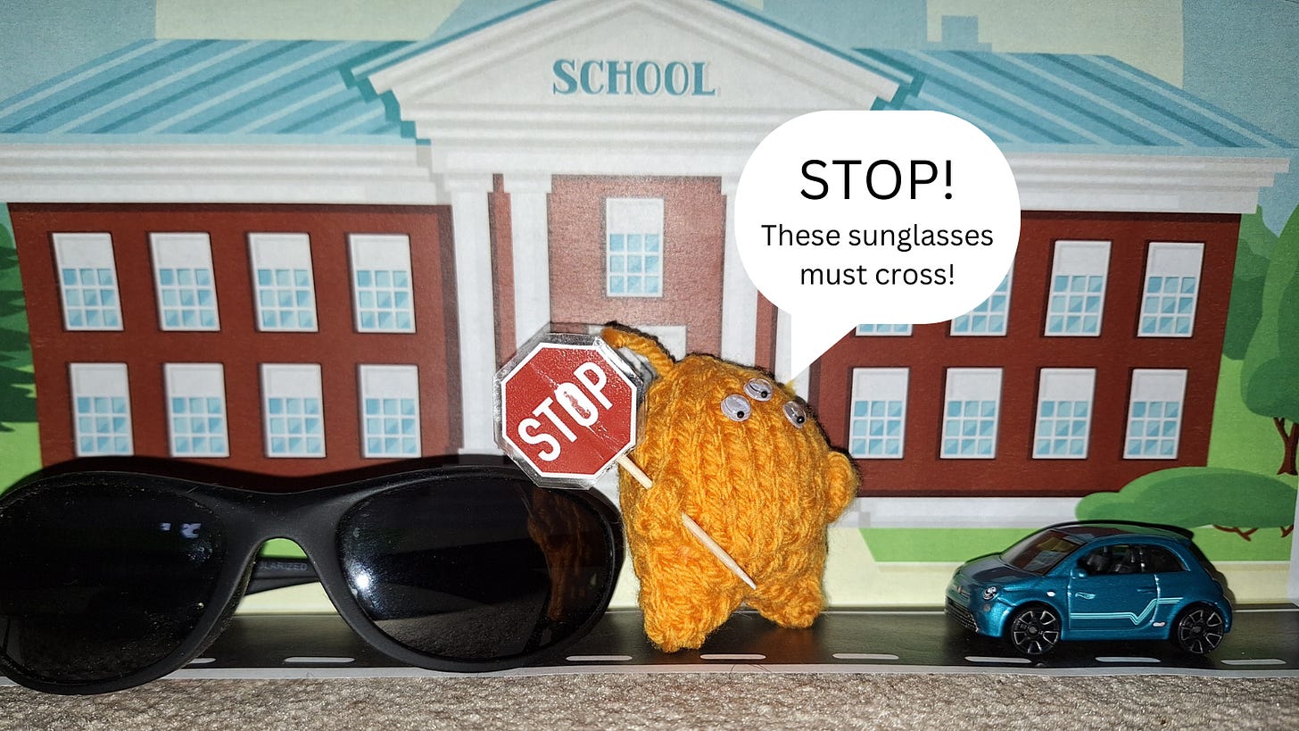 a pair of sunglasses. a knitted alien with a stop sign stopping a toy car in front of a print out of a school.