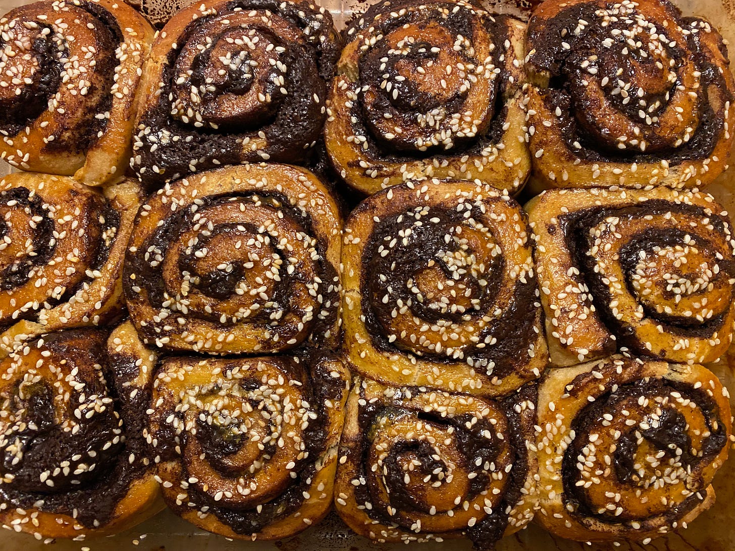 Closeup of a pan of golden-brown chocolate swirl buns sprinkled with sesame seeds.