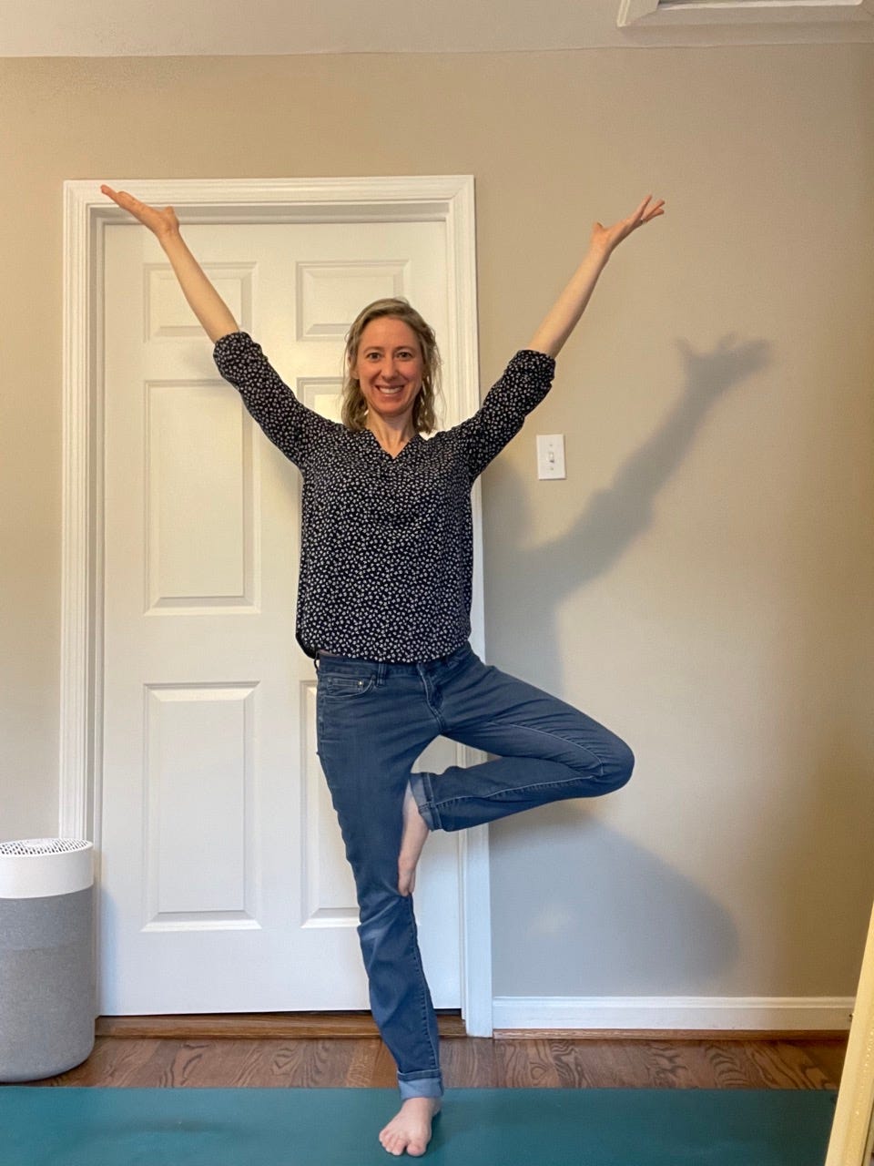 A woman in Tree Pose, smiling at the camera, arms open to the sky