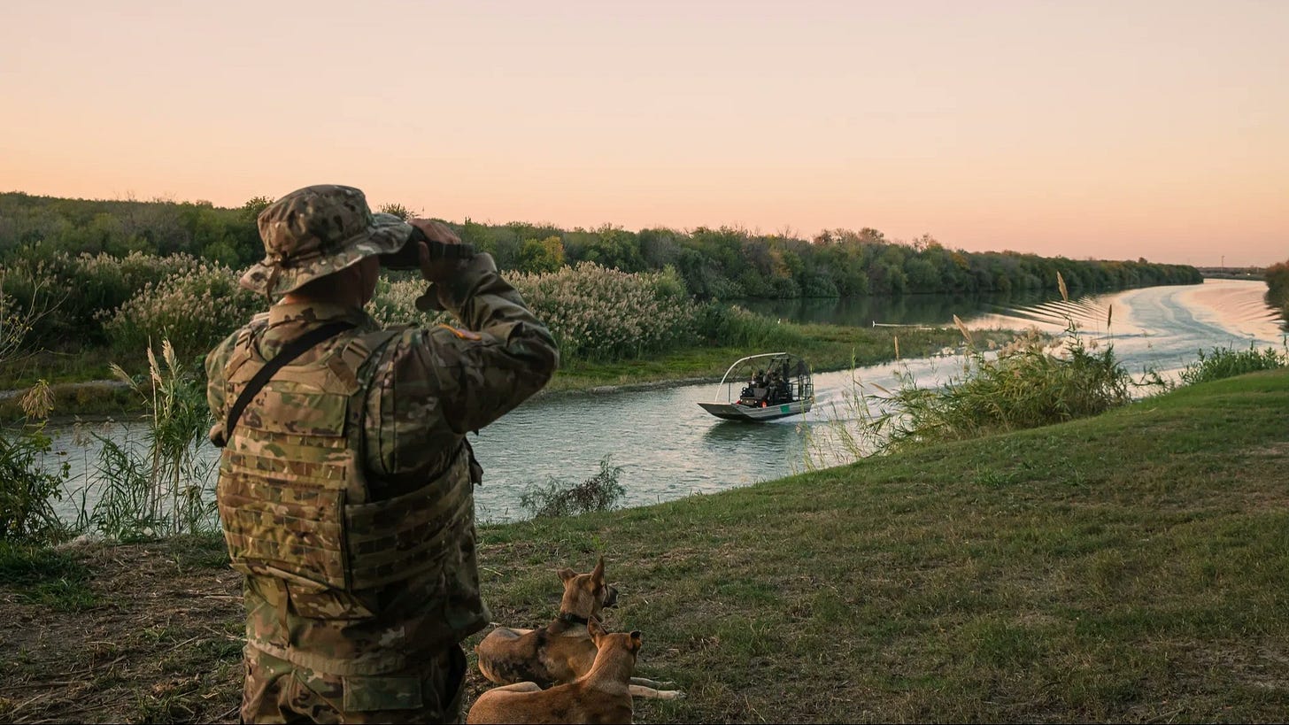 Texas National Guardsman maintains watch over Rio Grande as a state patrol boat passes by - in an effort to deter illegal crossings.