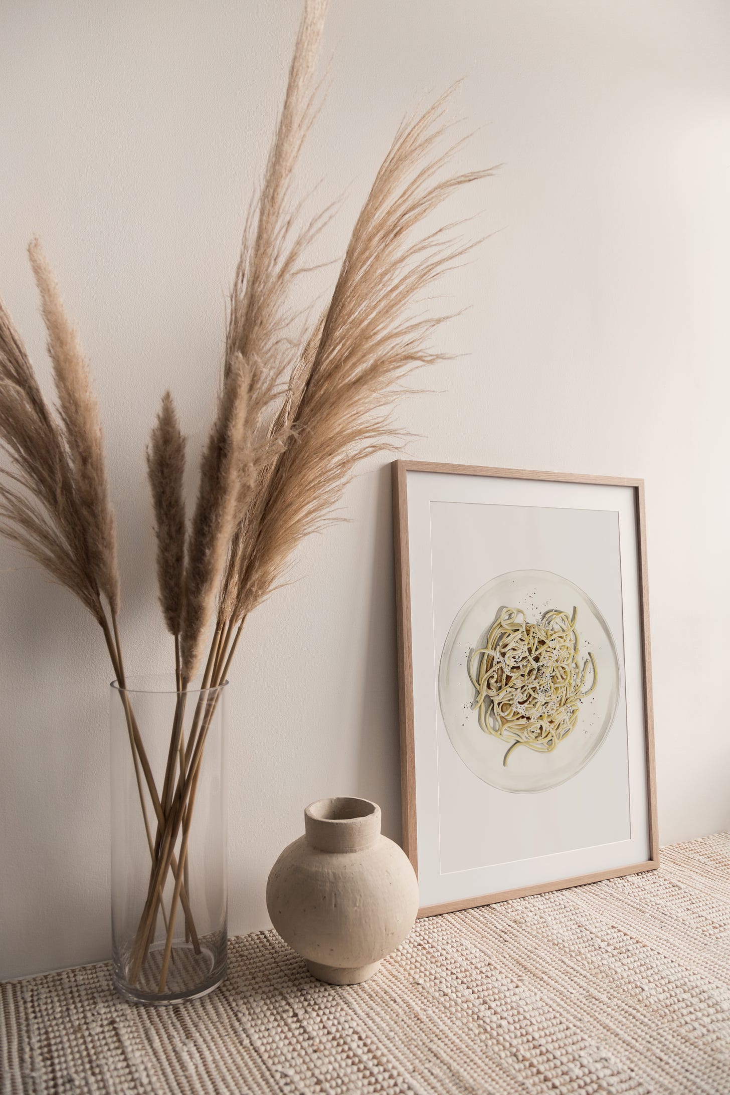A framed print of the cacio e pepe painting sitting on top of a shelf, with a vase of flowers to the left. 