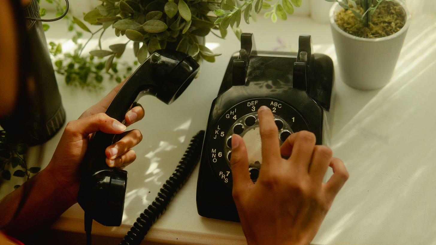 image of black rotary dial phone with hand on receiver and other hand dialing