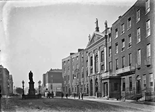 A black and white photo of a street with a statue and a building

Description automatically generated