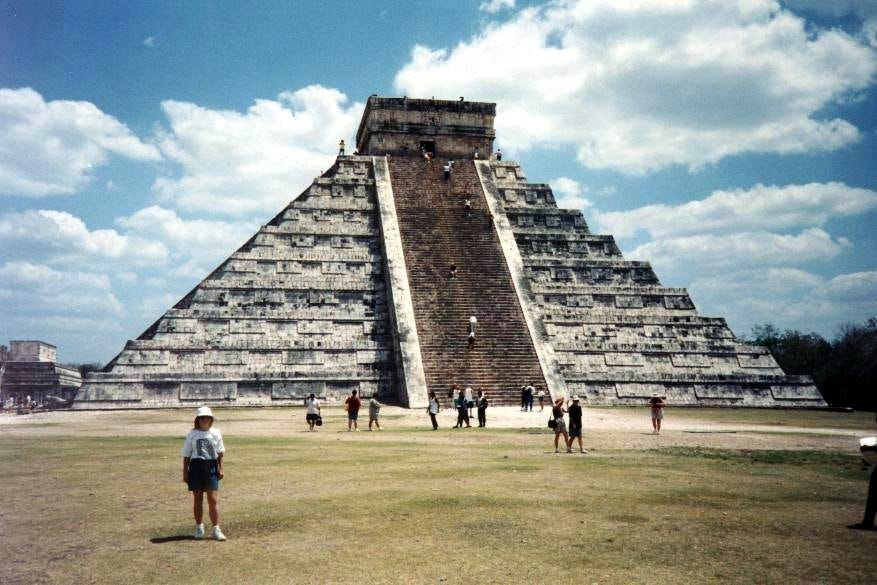 old photo of the Castillo of Chichen Itza with people climbing it