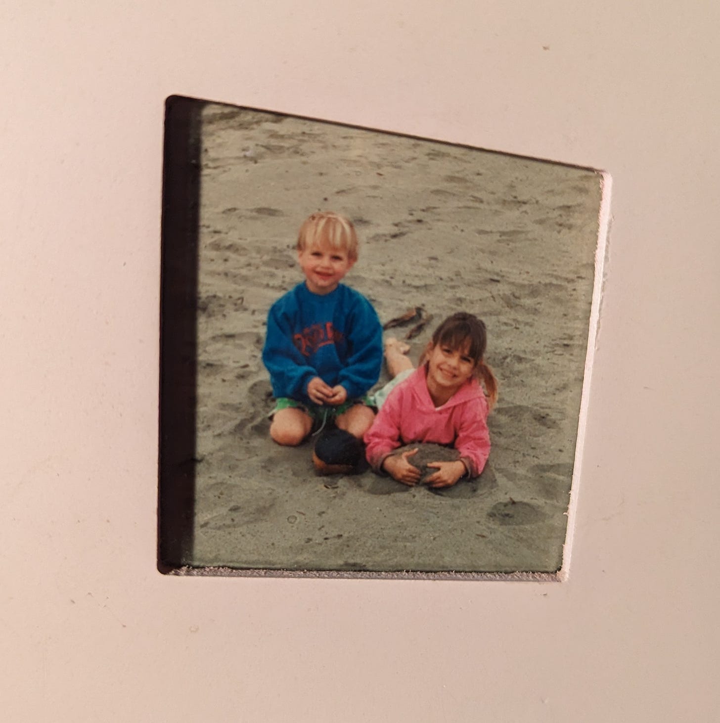 young brother and sister smiling in sand playing at beach