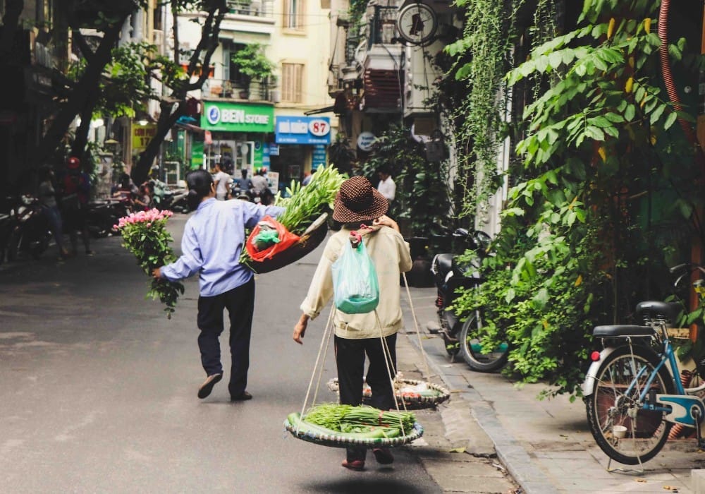 Asian couple carrying fresh flowers and food down a city street in Vietnam