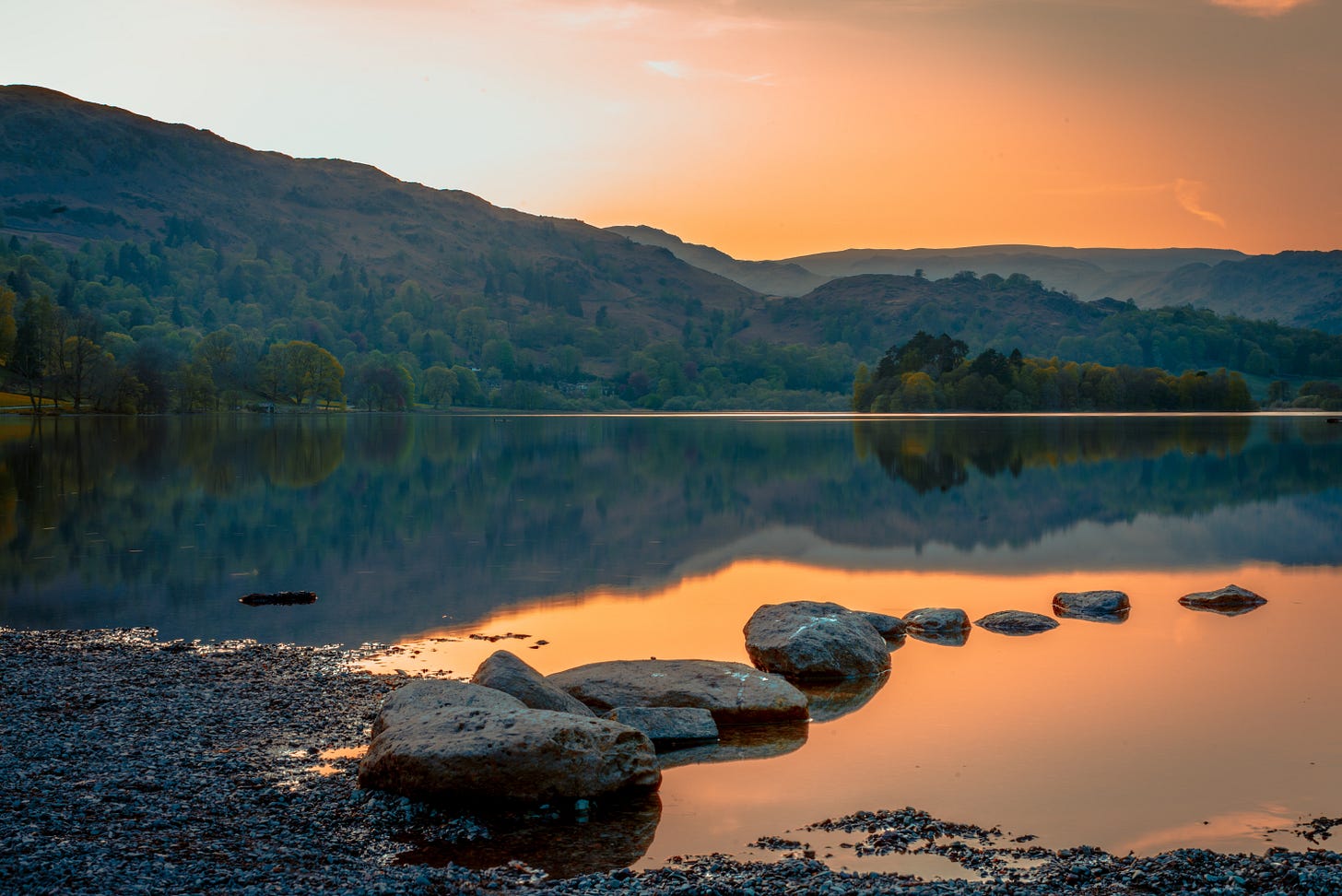 stepping stones leading to a lake, hills in the distance and orange sunset skies