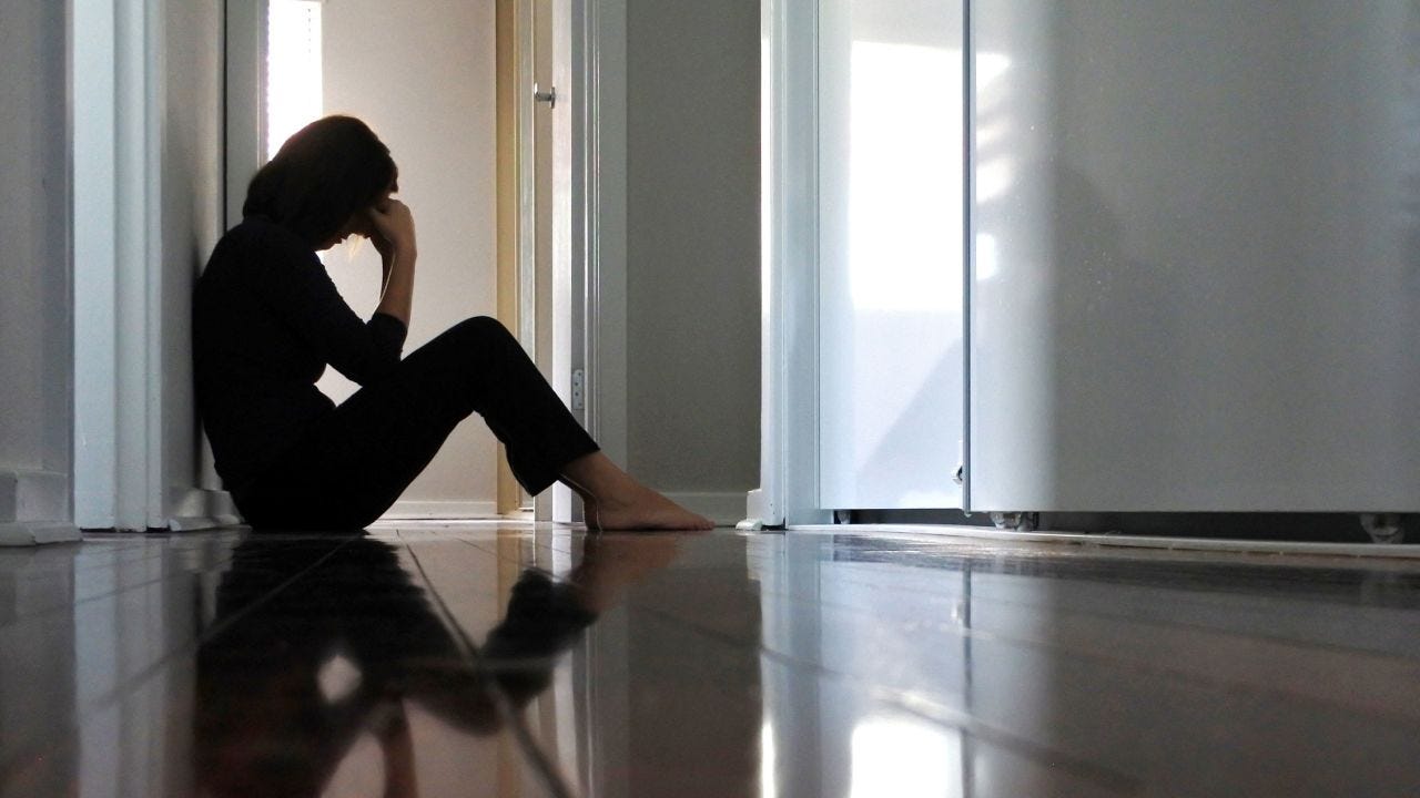 Sad adult woman sitting on dark home corridor floor.