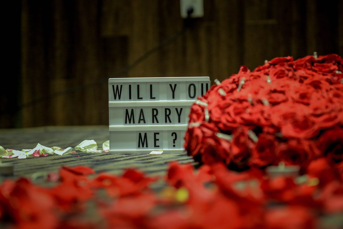 A sign that says "Will you marry me?" in block letters, next to a large bouquet of roses
