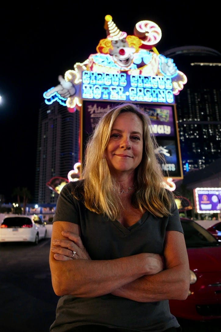 Woman standing in front of a colorful neon sign. Her arms are folded across her chest, and she's looking knowingly into the camera.