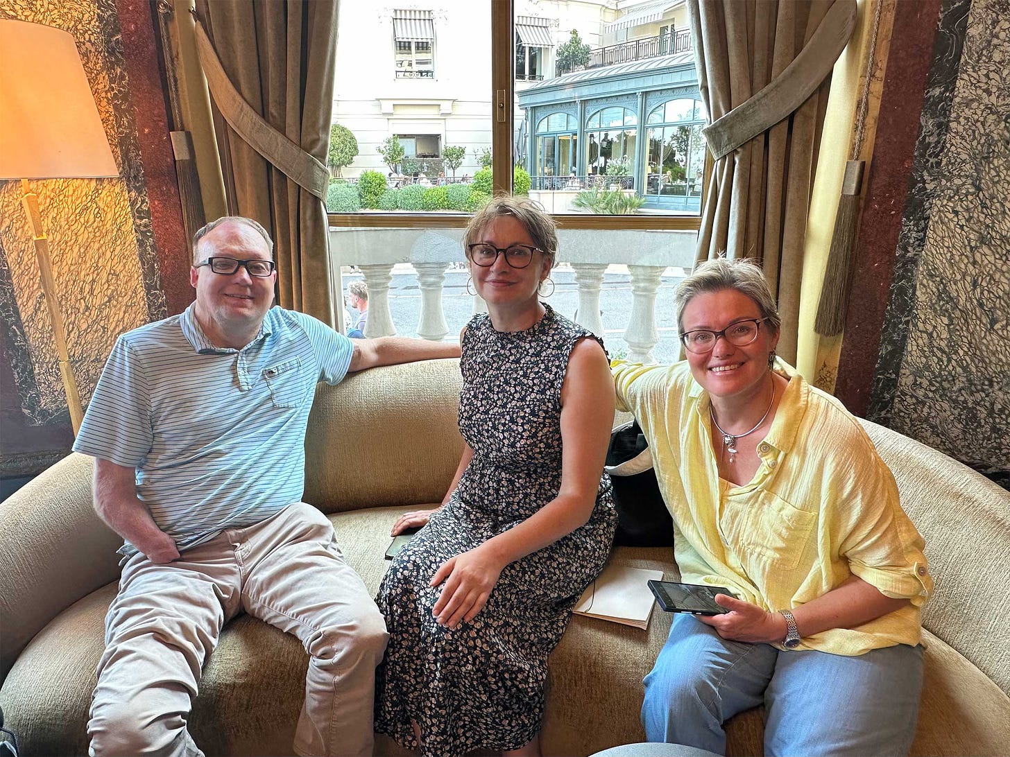 John seated on a sofa in a cafe with two women in Monaco.