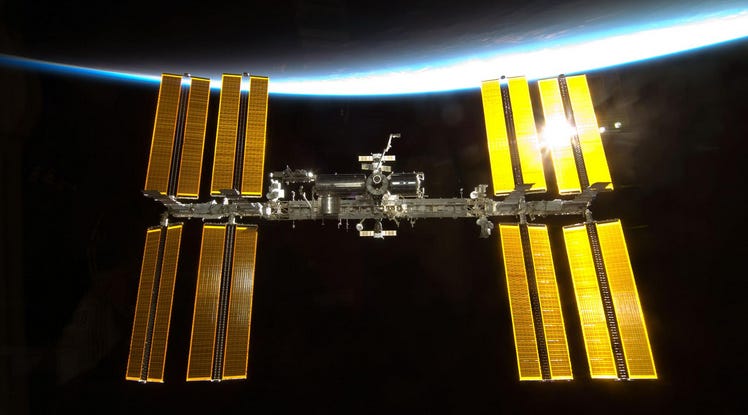 Image of the ISS with golden solar panels lit by the light of Earth.