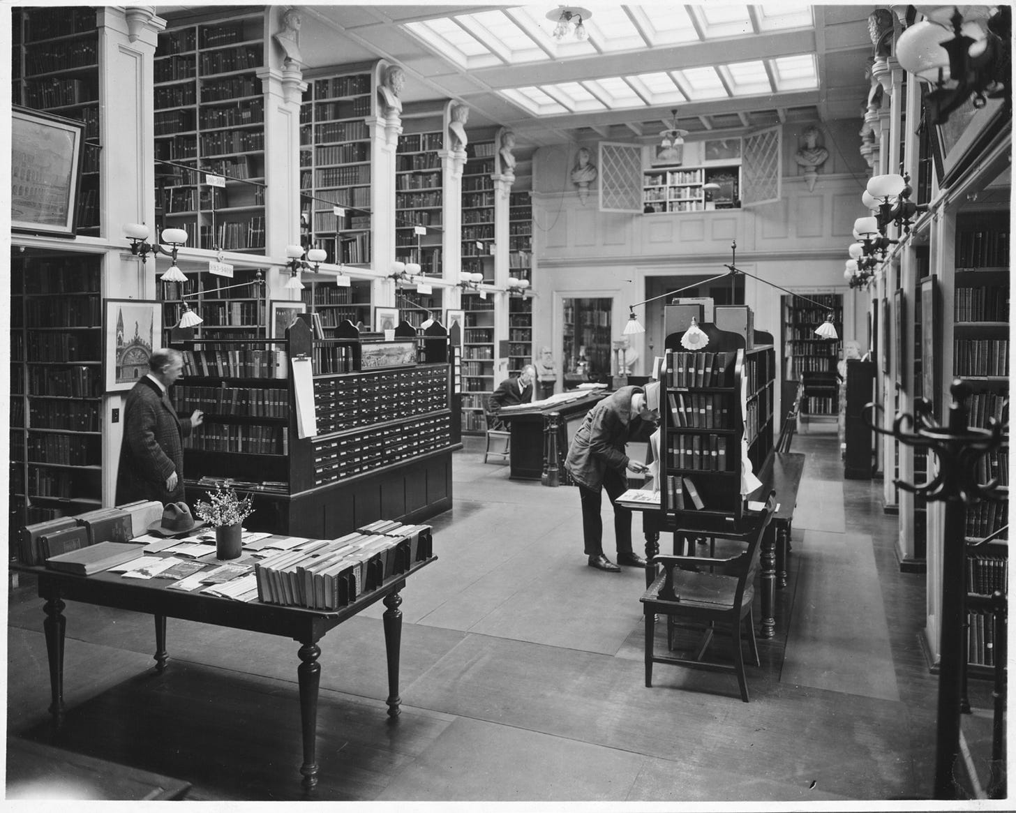 A historic, black-and-white photograph of patrons browsing books at the Providence Athenaeum library in 1918.