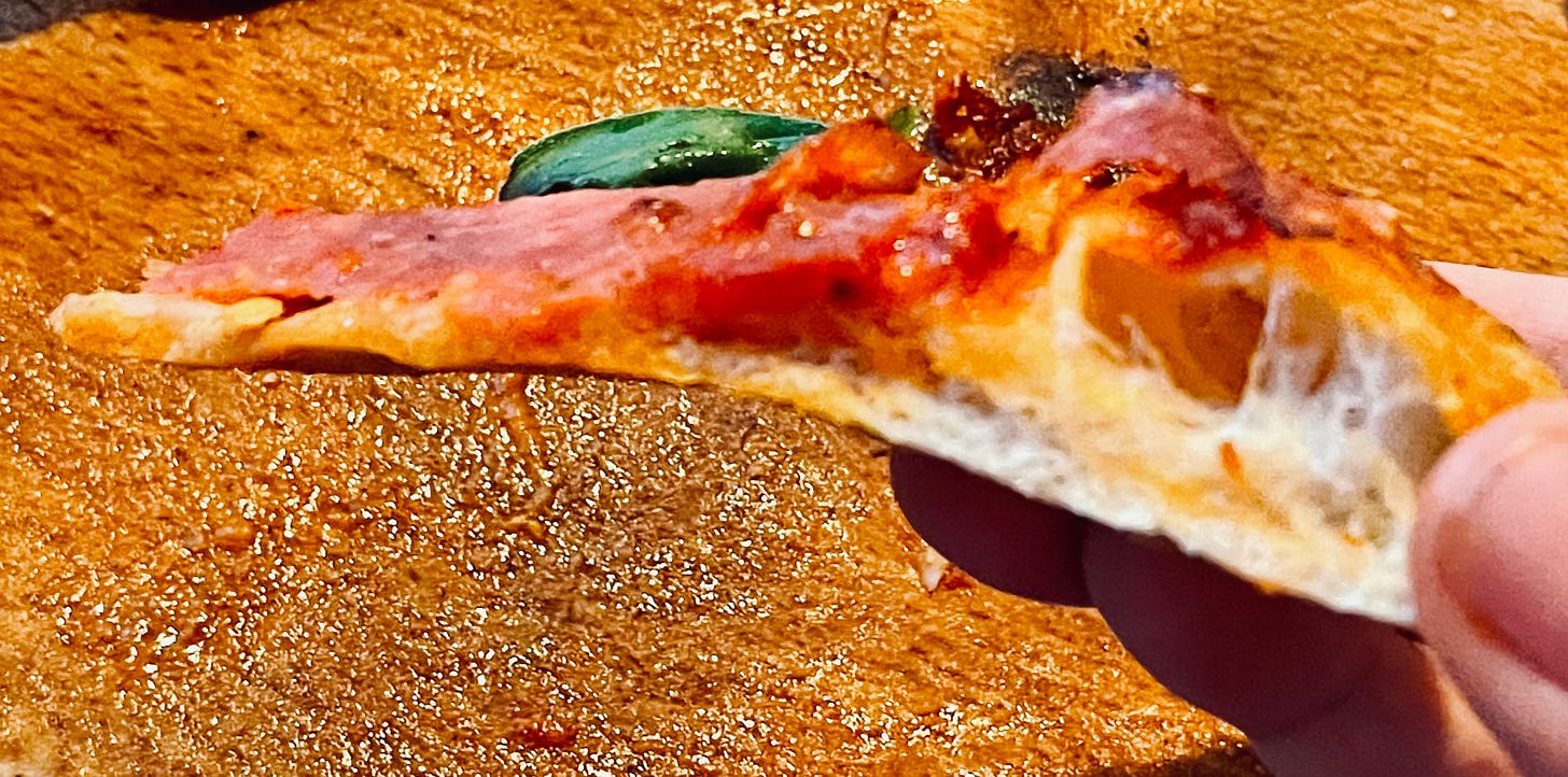 A side view of a single pizza slice being held up, with a crispy, golden crust and layers of tomato sauce, salami, and cheese, maintaining its shape even when lifted - 15 Minutes after having come out of the oven! A side view of a single pizza slice being held up, with a crispy, golden crust and layers of tomato sauce, salami, and cheese, maintaining its shape even when lifted - 15 Minutes after having come out of the oven!