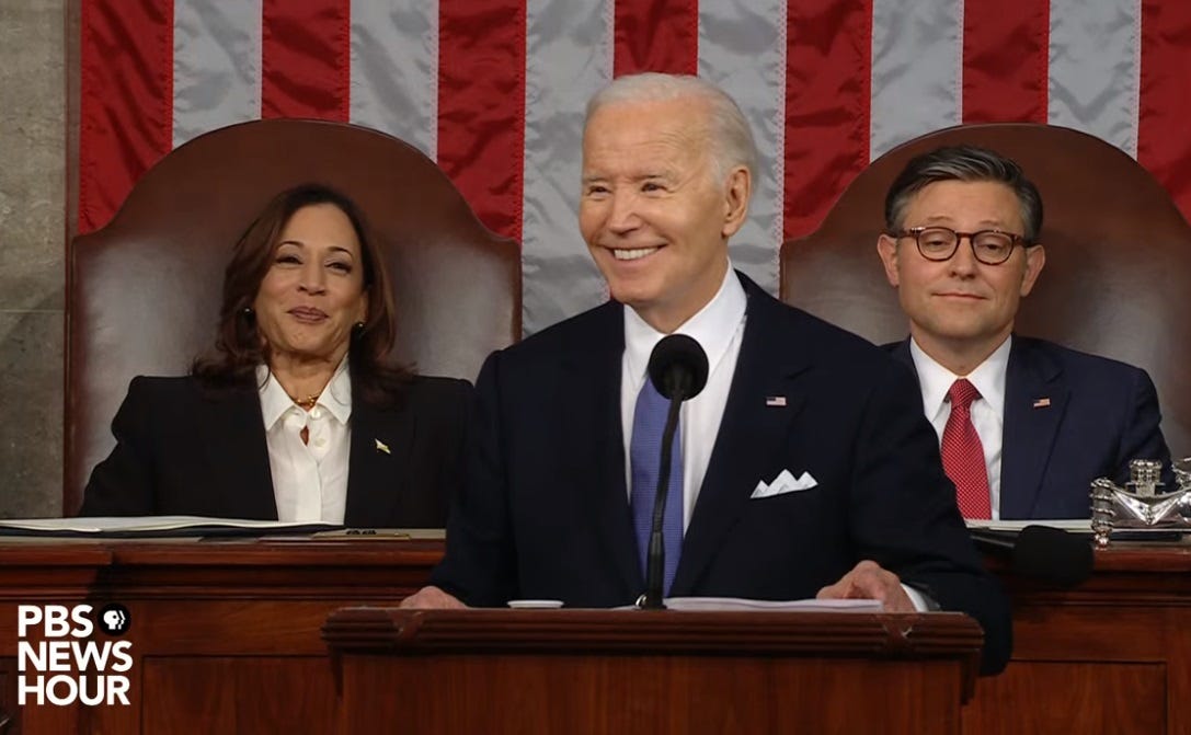 Video screenshot of a smiling Joe Biden during his 2024 State of the Union address, with Kamala Harris smiling as well, and Mike Johnson looking ... gassy.