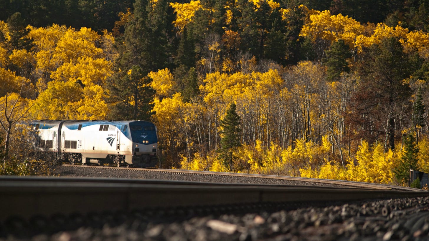 Empire Builder train passing through a forested area with fall foliage.