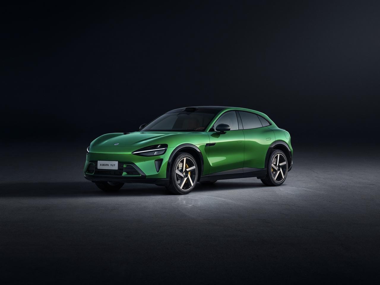 A green electric SUV is parked in front of a dark background. The car's design is modern, with a unique front end, and the tires contrast sharply with the color of the vehicle.