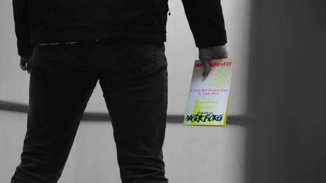 A man in black clothing seen from behind. His ass is fantastic. In his hands he holds a copy of MORK KOPHETS. The image is in black and white but the zine is bright yellow.